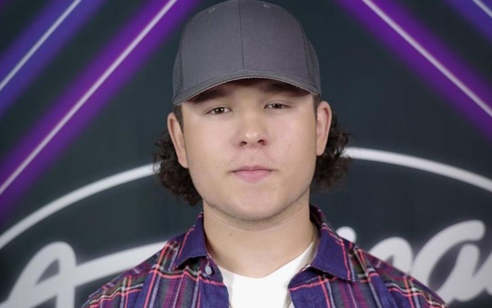 Caleb Kennedy usando boné em frente a letreiro do American Idol