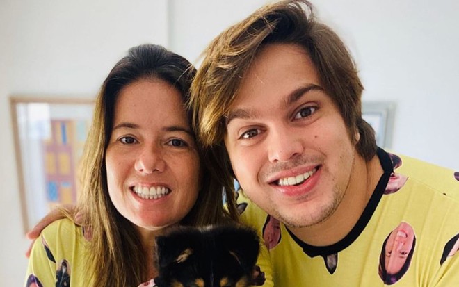 Na foto, Camila sorri e usa camiseta amarela com o rosto de Lucas estampado; Lucas está abraçado com a esposa e usa uma camiseta igual com o rosto dela