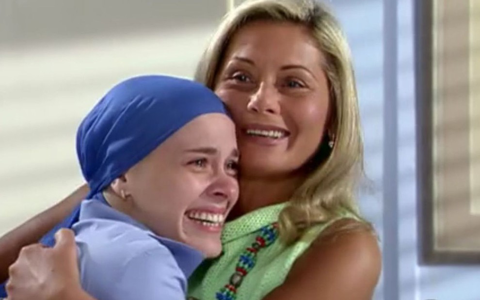 Carolina Dieckmann de lenço azul na cabeça, sorridente, abraçada a Vera Fischer, de blusa verde, em cena de Laços de Família