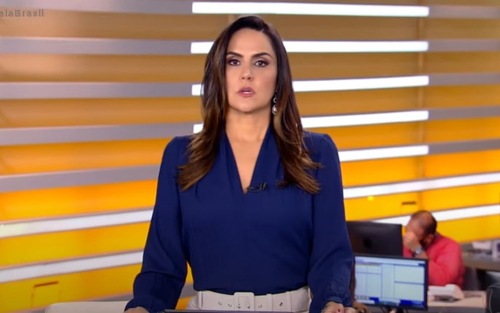 A jornalista Carla Cecato em cenário do telejornal Fala Brasil, da Record; ela usa blusa azul marinho e tem cabelo penteado para o lado