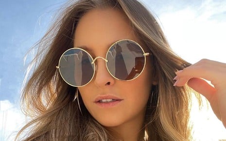 Carla Diaz posa para selfie com o céu ensolarado e óculos de sol redondos