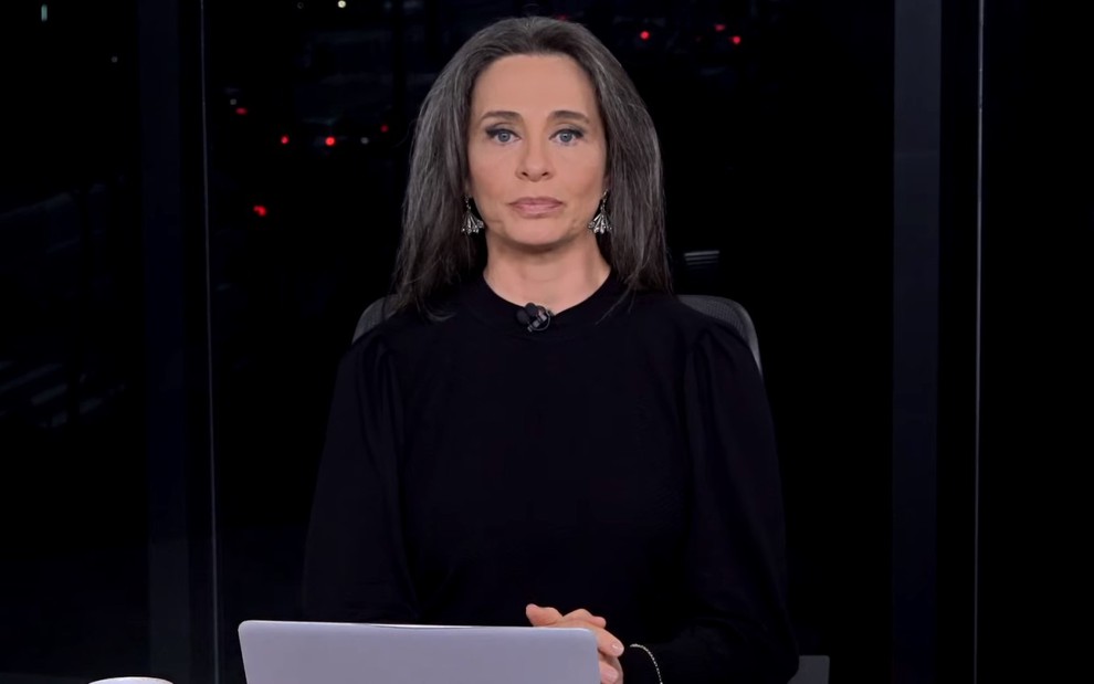 Carla Vilhena com uma blusa preta em um cenário escuro em telejornal da CNN Brasil