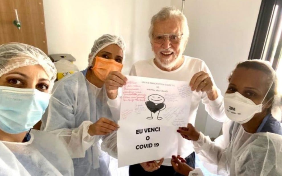 Carlos Alberto de Nóbrega segura um cartaz escrito 'eu venci a Covid-19' em foto ao lado de profissionais de saúde