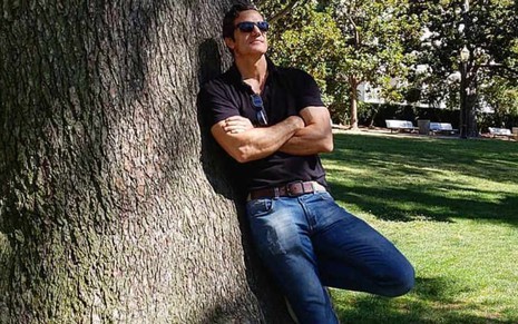 O ator Carlos Machado encostado numa árvore, em paisagem bucólica, em foto publicada em seu perfil no Instagram