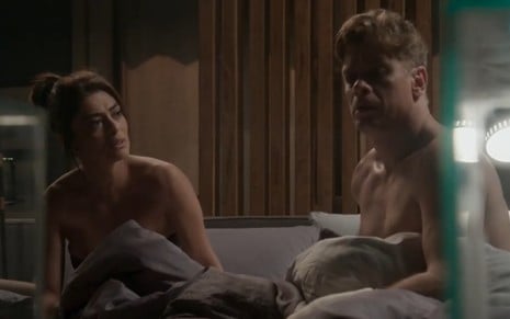 Sentada na cama, a atriz Juliana Paes (Carolina) olha com cara de reprovação para Fabio Assunção (Arthur), que está triste