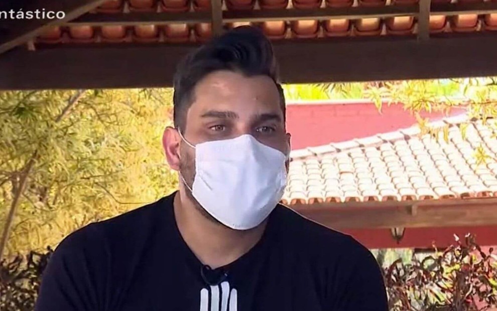 Com uma máscara branca, o sertanejo Cauan concede entrevista para o Fantástico
