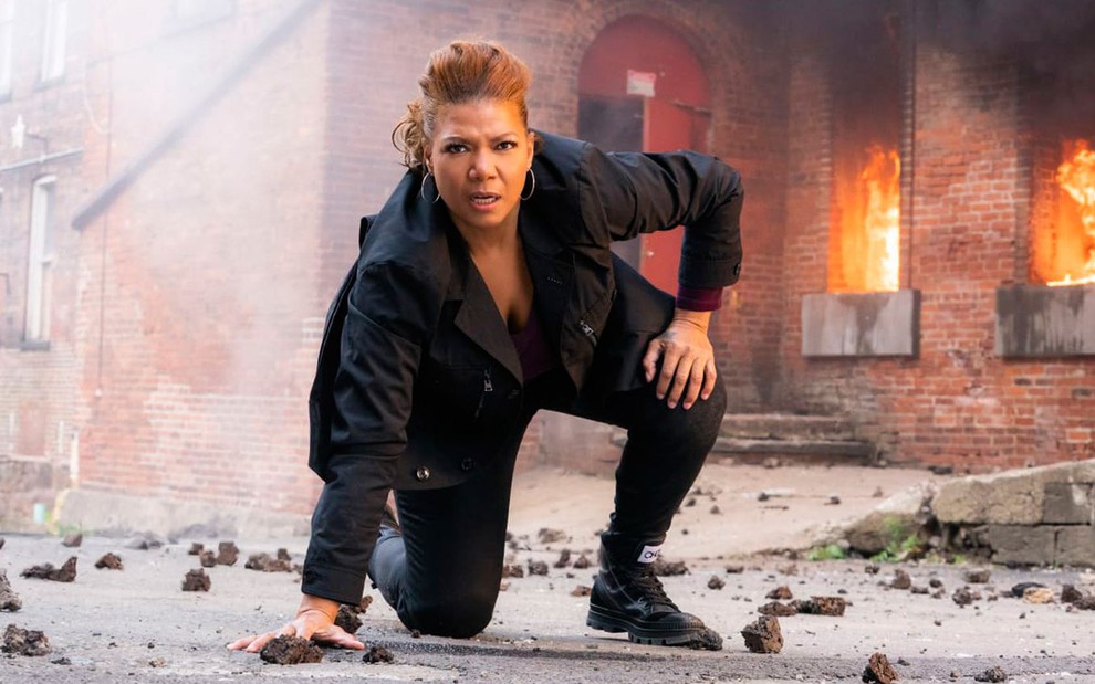 Queen Latifah está agachada no chão na frente de um prédio em chamas na série The Equalizer