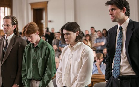 Um homem engravatado à direita e dois meninos ao centro com a cabeça abaixada no que parece ser um julgamento; além de outro homem engravatado à esquerda