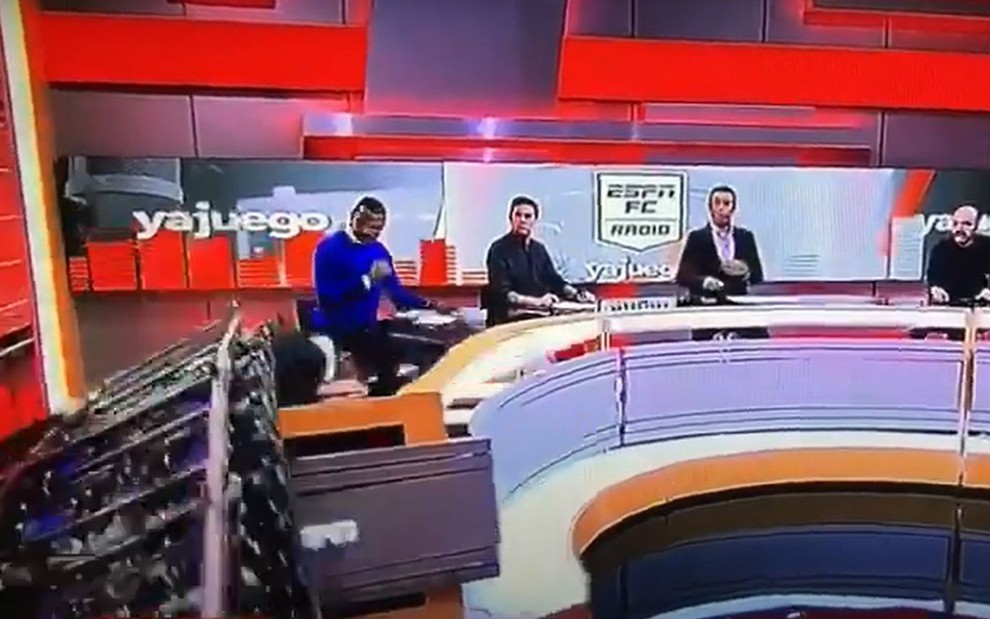 Carlos Orduz debruçado na bancada do programa ESPN Radio Colombia, com parte do cenário em cima dele