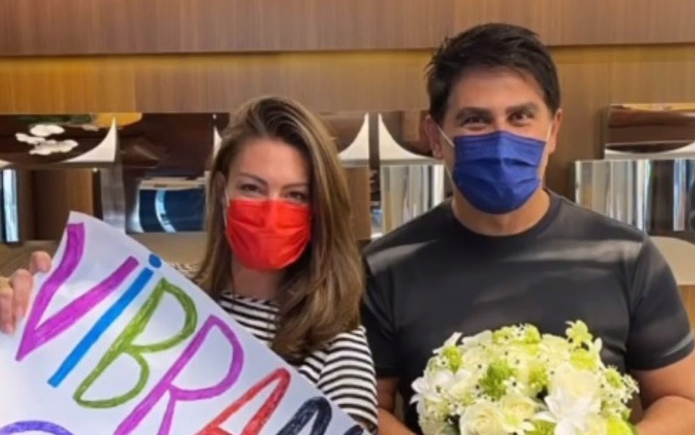 Elaine Mickely e Cesar Filho de máscara na recepção de hospital em São Paulo; ele está segurando flores