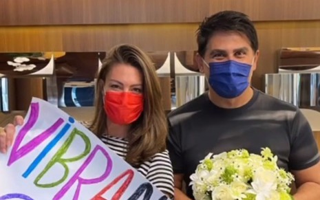 Elaine Mickely e Cesar Filho de máscara na recepção de hospital em São Paulo; ele está segurando flores
