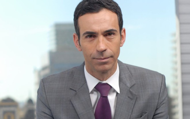 O apresentador César Tralli na bancada do SP1, da Globo, usando terno cinza e gravata roxa