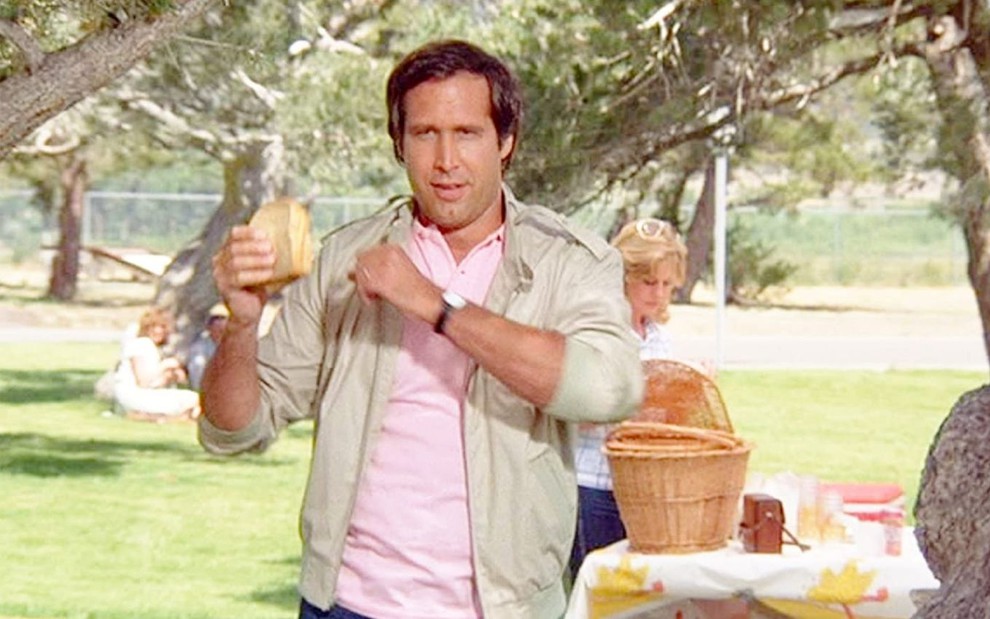 Chevy Chase come em piquenique em cena de Férias Frustradas (1983)
