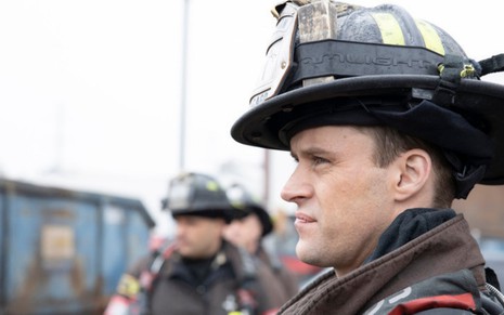 Com capacete e roupa de bombeiro, o ator Jesse Spencer aparece para apagar um incêndio na série Chicago Fire