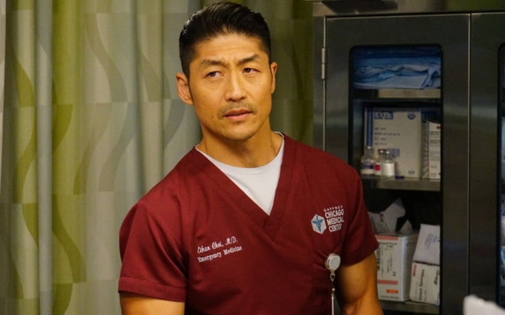 Com um uniforme de cor grená e dentro do um quarto hospitalar, Brian Tee aparece na série Chicago Med