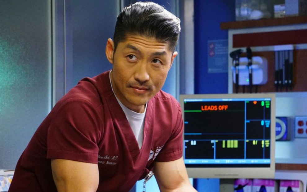Dentro de um quarto de um hospital, o ator Brian Tee veste uma roupa grená na série Chicago Med
