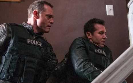 Com coletes à prova de balas, Jason Beghe e Jon Seda sobem de mansinho uma escada em cena de Chicago P.D.