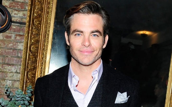 Chris Pine vestindo term preto e camisa branca posando para foto em frente a um quadro