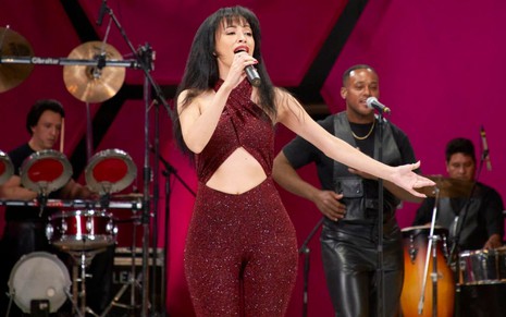 Christian Serratos usa um macacão vermelho brilhoso e canta em cena da segunda parte de Selena: A Série