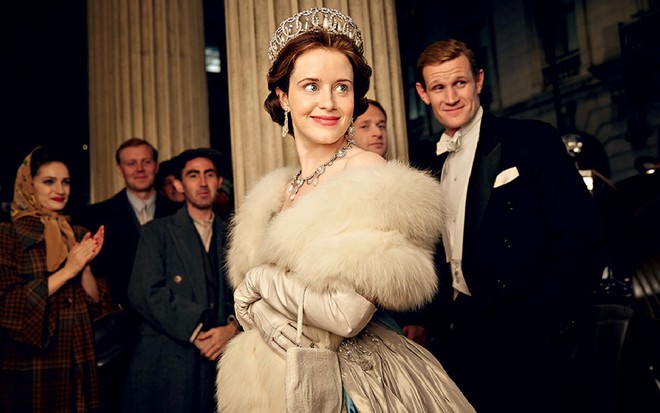 Claire Foy no papel da jovem rainha Elizabeth, com roupa de gala clara e coroa na cabeça e dando um leve sorriso com rosto virado para o lado