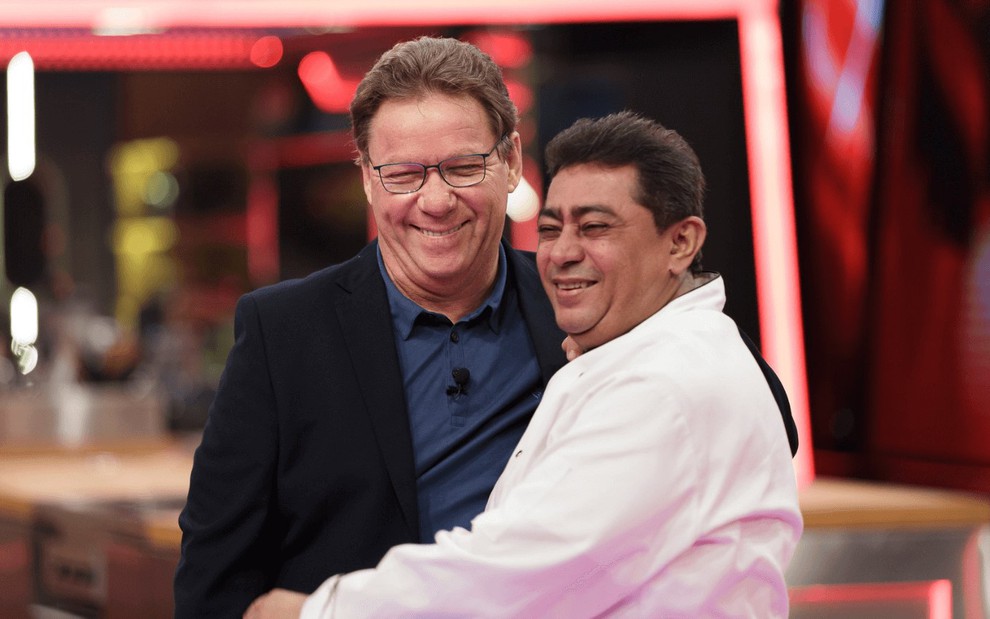 Claude Troisgros e Batista abraçados e sorridentes no cenário do reality show Mestre do Sabor