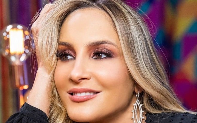 Claudia Leitte posando de blusa preta de manga longa, com a mão apoiada na cabeça