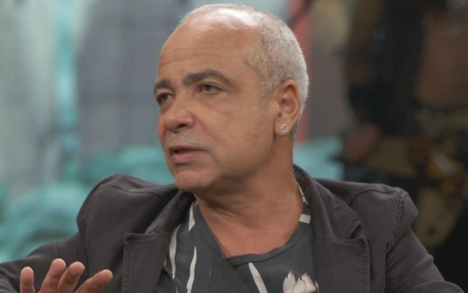 Claudio Manoel sentado de blazer cinza