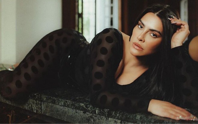 Cleo deitada usando um vestido preto e decotado