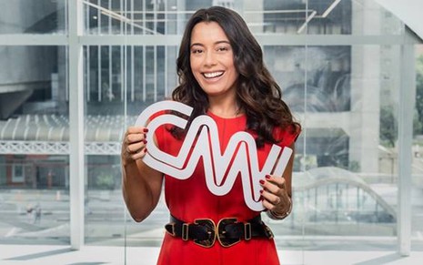 A jornalista Daniela Filomeno sorridente, de vestido vermelho segurando o logo da CNN