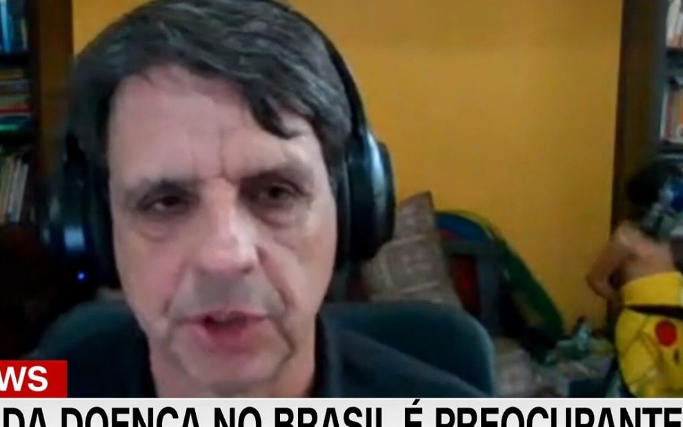 Professor da PUC, Silvio Camacho dá entrevista para a CNN enquanto o filho mais novo coloca uma capa de Pikachu