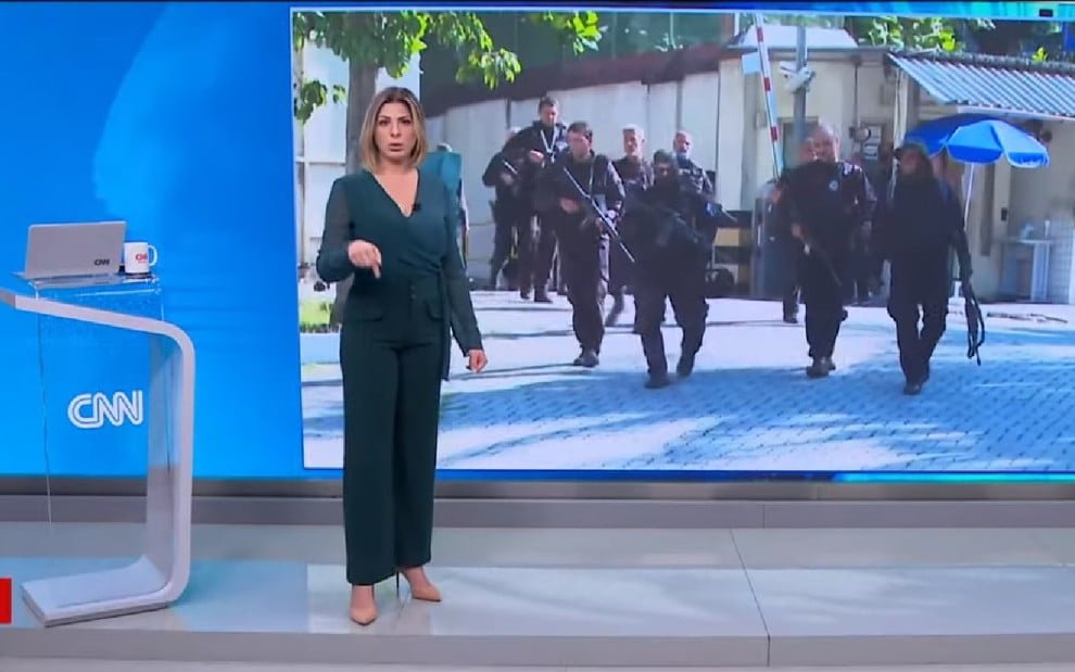 Daniela Lima em pé no programa CNN 360 diante de telão com imagem de policiais