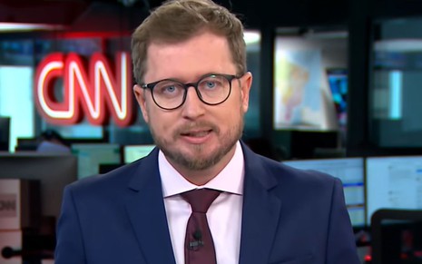 O jornalista Leandro Narloch com expressão séria, terno azul e gravata roxa na Redação da CNN Brasil