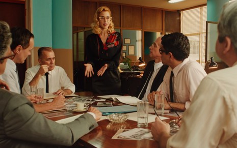 Mel Lisboa em Coisa Mais Linda; rodeada de homens, a jornalista Theresa argumenta a favor do seu trabalho