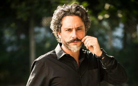 Ator Alexandre Nero interpreta o Comendador José Alfredo na novela Império. Na foto, ele usa camisa preta e mexe no bigode.