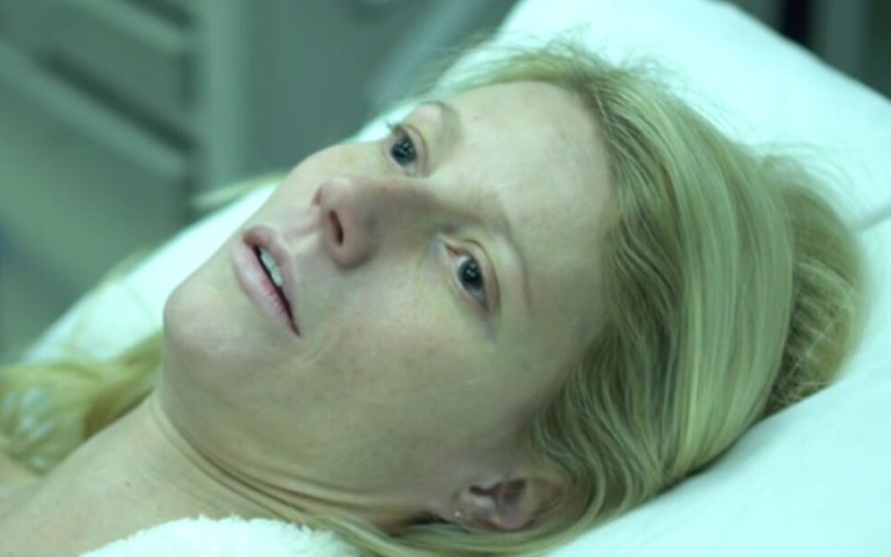 Gwyneth Paltrow como a personagem Beth Emhoff no filme Contágio: ela está deitada em uma maca, pálida e com olhos abertos