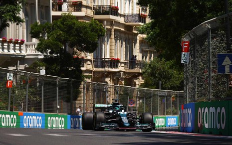 Carro de Fórmula 1 no meio de uma curva na pista do circuito de rua com detalhes de grades nas laterais e casas e árvores ao fundo