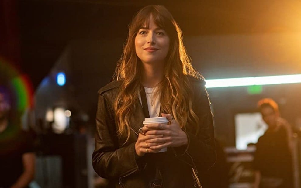 Dakota Johnson sorri e segura um copo de café em cena como Maggie Sherwood em A Batida Perfeita (2020)