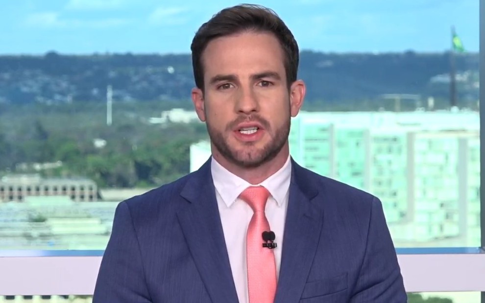 Daniel Adjuto com uma gravata rosa e terno azul na bancada de um telejornal da CNN Brasil