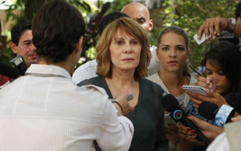 A atriz Renata Sorrah (Danielle) com expressão de desespero enquanto é cercada por jornalistas em cena da novela Fina Estampa