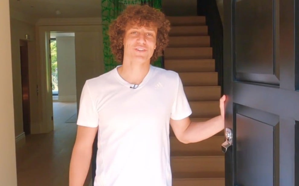 David Luiz de camiseta branca, segurando uma porta preta e sorrindo