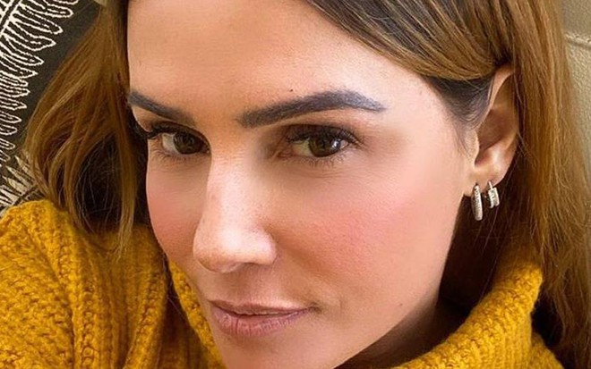 Deborah Secco em selfie tirada com o cabelo solto e uma blusa de gola alta na cor mostarda