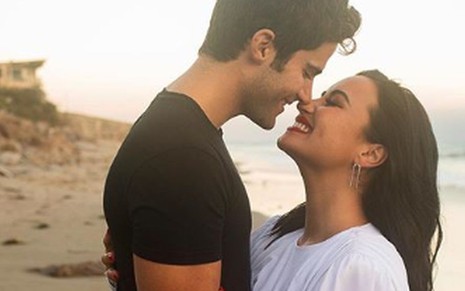 Demi Lovato e Max Ehrich frente a frente, prestes a se beijarem em frente ao mar