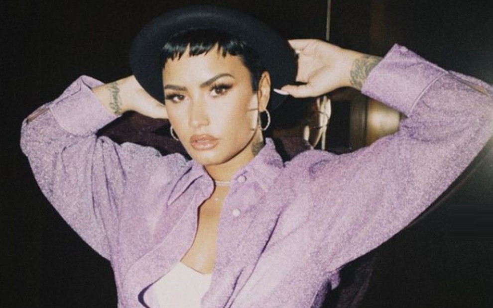 A cantora Demi Lovato posa para foto usando casaco roxo e chapéu preto