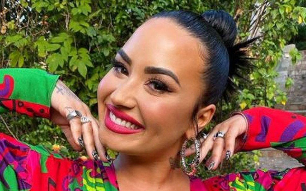 Demi Lovato de cabelo preso, vestido nas cores verde e vermelha, com batom combinando