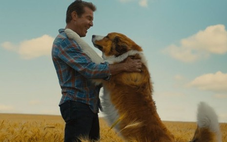 O personagem Ethan (Dennis Quaid) está em pé e abraça o cachorro Bailey em cena de Quatro Vidas de um Cachorro (2017)