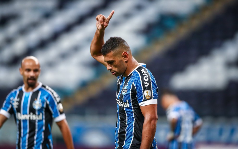 O jogador do Grêmio, Diego Souza, comemora gol em campo, com dedo indicador apontado para cima, vestido com o uniforme do time nas cores azul, preto e branco