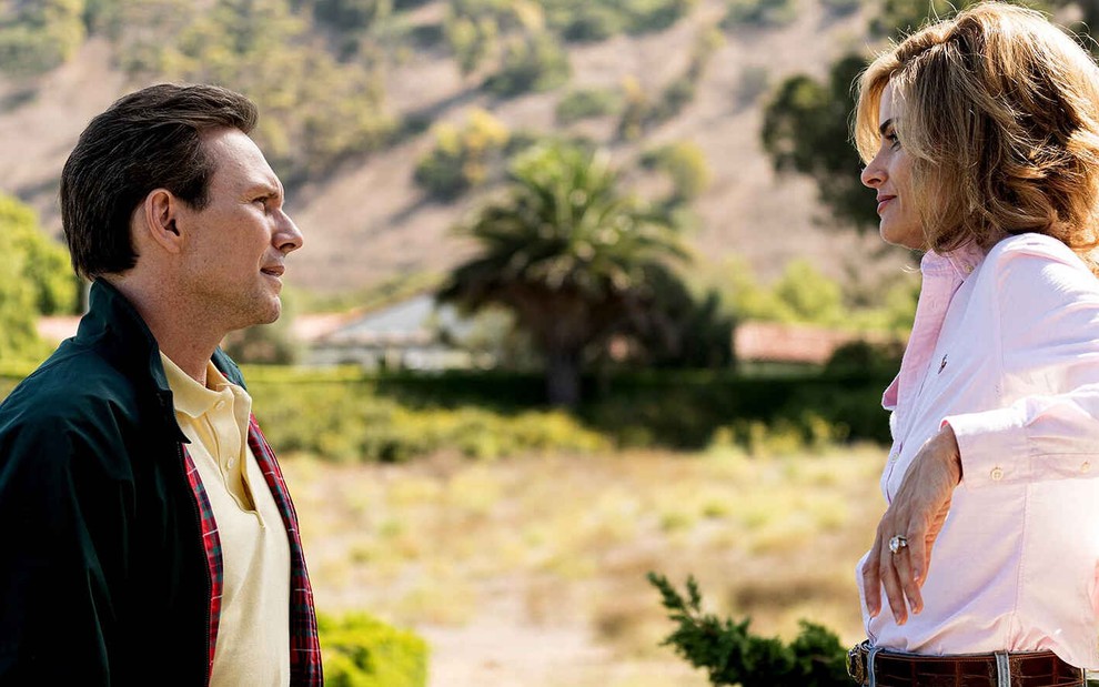 Em um ambiente verdejante, os atores Christian Slater e Amanda Peet trocam olhares em cena de Dirty John
