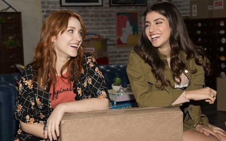 Imagem em que as personagens Helena/Ana e Bia riem sentadas em uma poltrona na série Bia, do Disney Channel