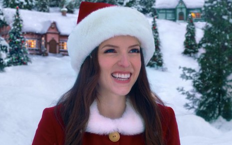 A atriz Anna Kendrick usa um gorro de Papai Noel e trajes vermelhos em cena de Noelle (2019); ela sorri e está em um cenário coberto de neve