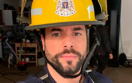 Pedro Carvalho em foto do bastidor de Amor Amor: caracterizado como o personagem Serafim, ator está vestido de bombeiro
